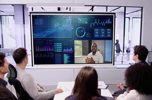 Photo of several people looking at a large monitor for a conference call.